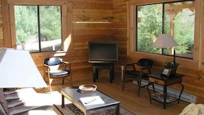 A cozy cabin interior with a sofa, a coffee table, a TV, and two chairs. - Texan Resort (Lake City)