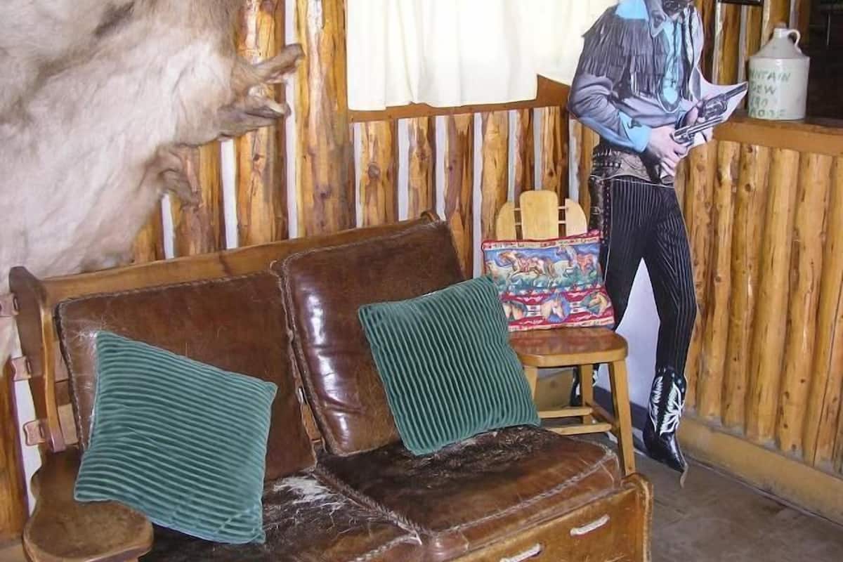 Interior rústico de una cabaña de madera con un sofá de cuero, una pequeña mesa de madera y un adorno en la pared.