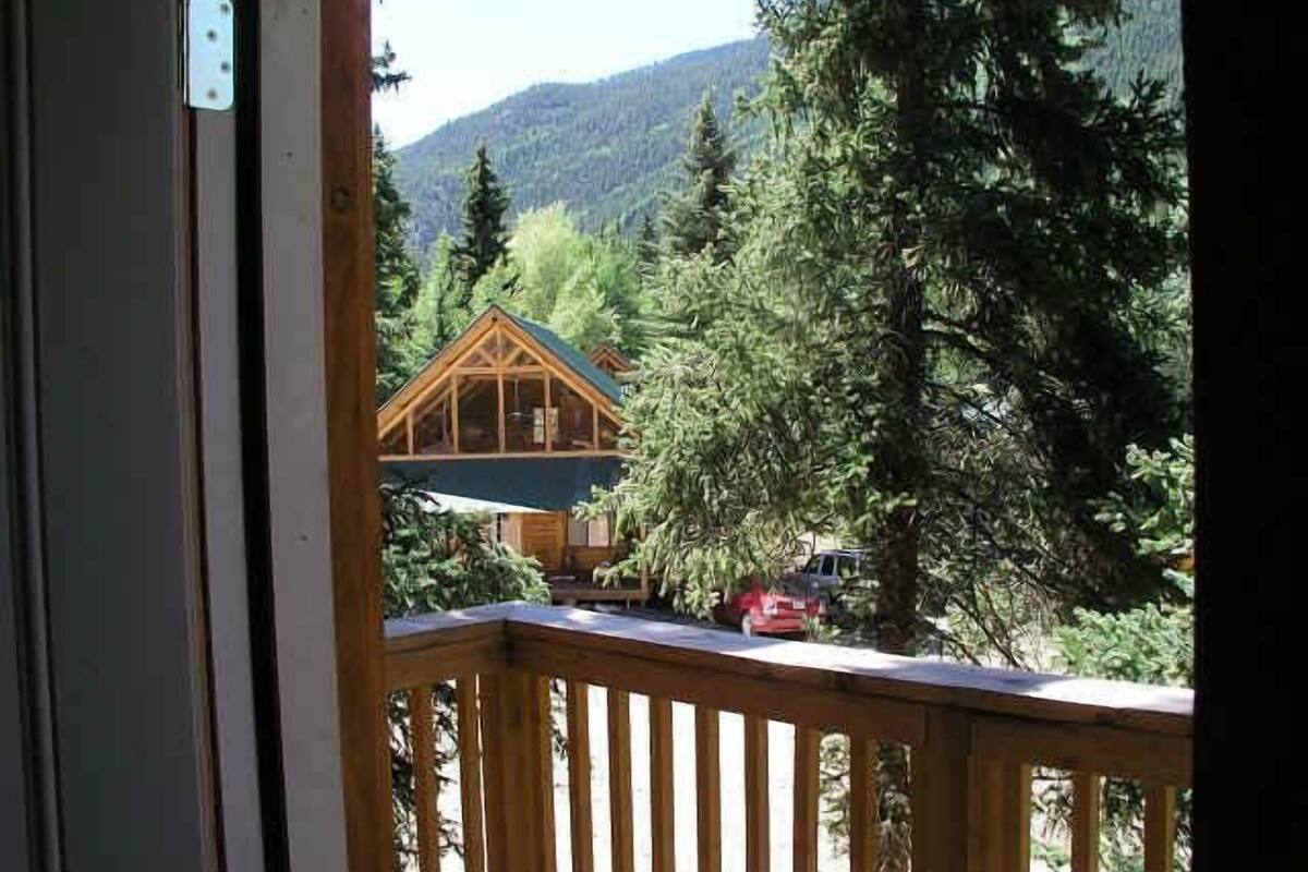 Una terraza de madera con vistas a una cabaña rodeada de árboles y montañas.