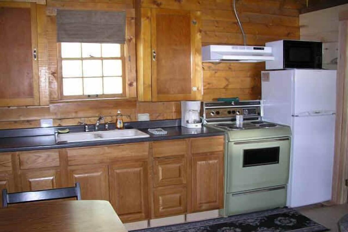Una cocina con armarios de madera, un lavamanos, una estufa y un microondas.