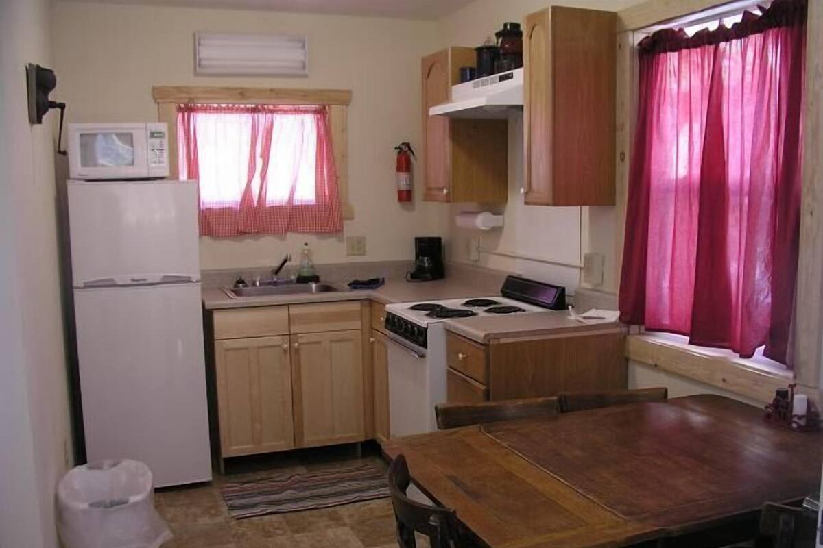 Cocina compacta con refrigerador, estufa, microondas y gabinetes de madera.