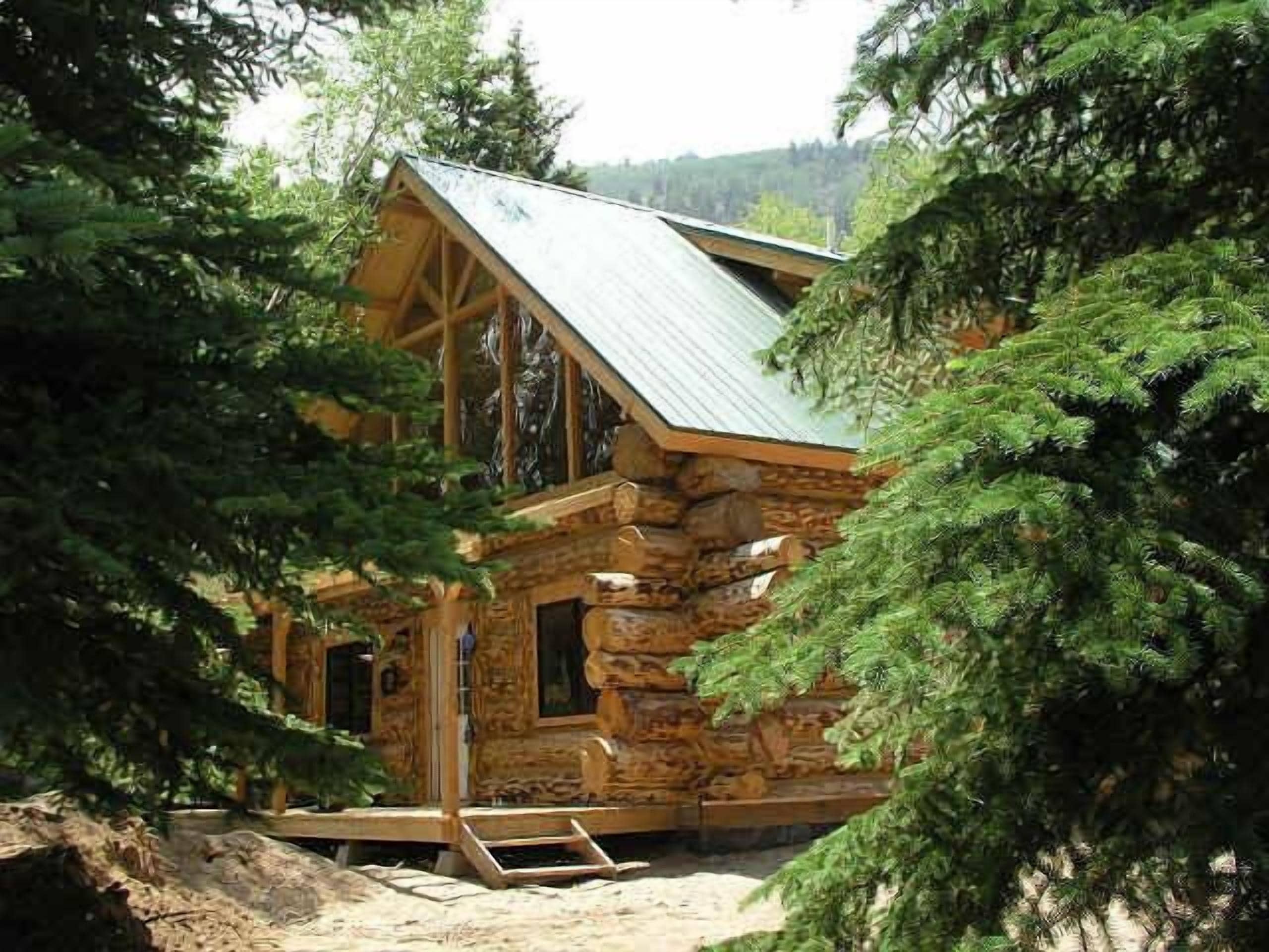 Une cabane rustique en rondins de bois, dotée d’un toit à forte pente, entourée d’une forêt dense.