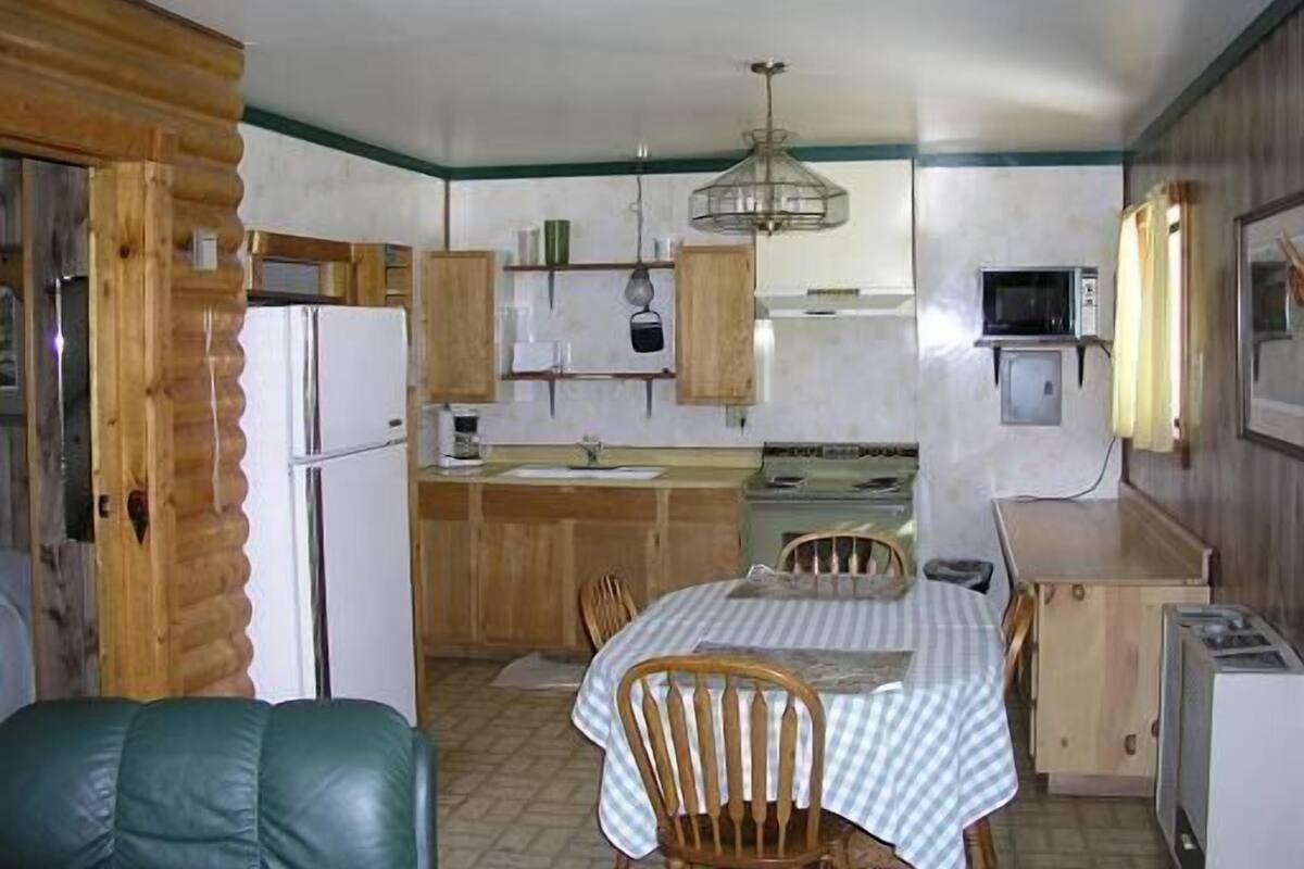 Una cocina compacta con armarios de madera, una mesa de comedor con sillas, un refrigerador y un microondas.