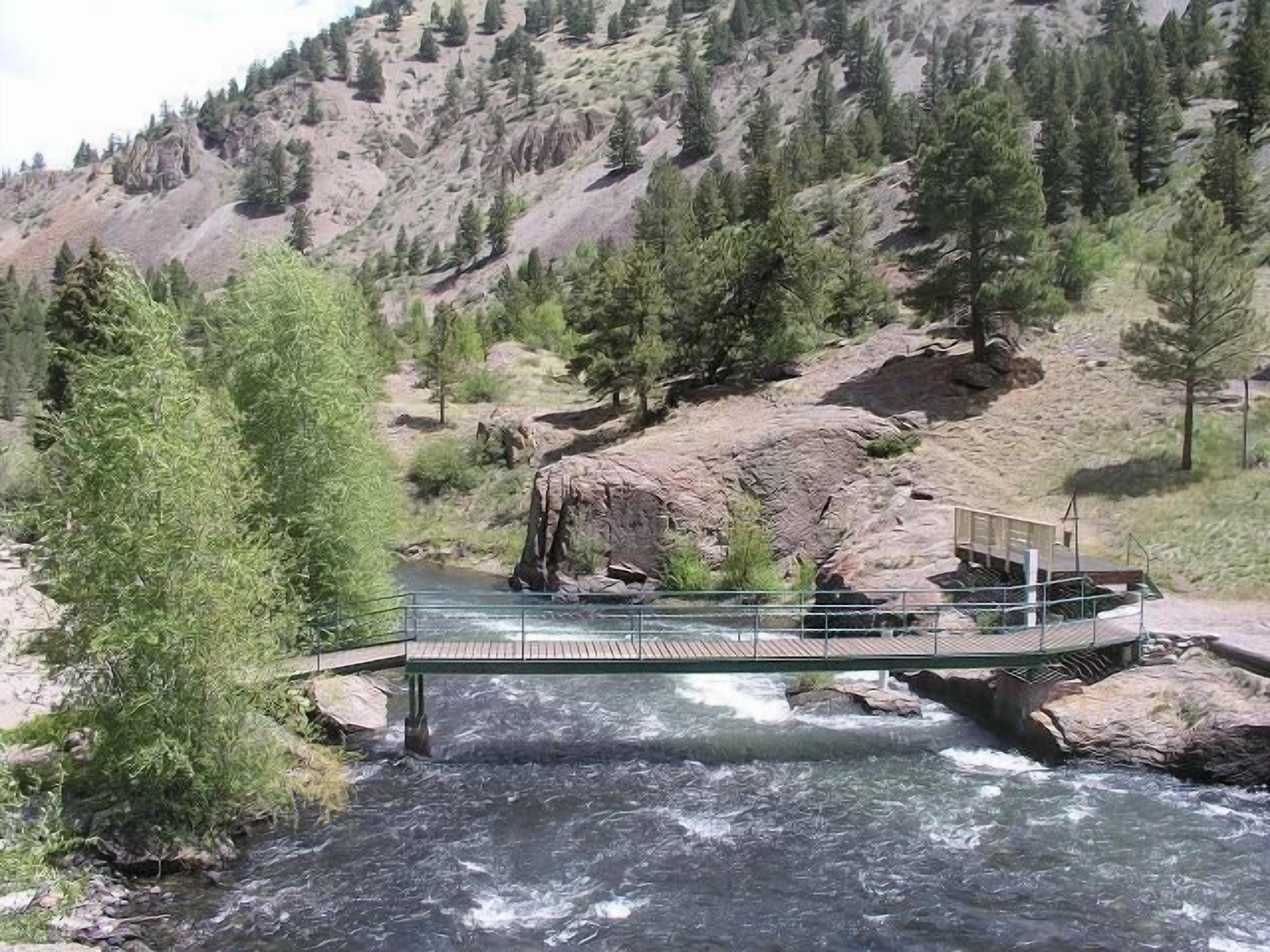 Un fiume con un ponte, circondato da alberi e terreno roccioso.