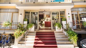A multi-story building with balconies, a red carpeted entrance, and potted plants.