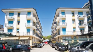 A row of two-story buildings with balconies, parked cars, and a clear blue sky.