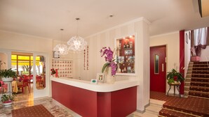 A hotel reception area with a red counter, a chandelier, and a mirror reflecting the interior.
