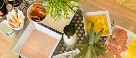 A buffet table with various food items, including a bowl of fruit, a dish of meat, and a container of condiments.