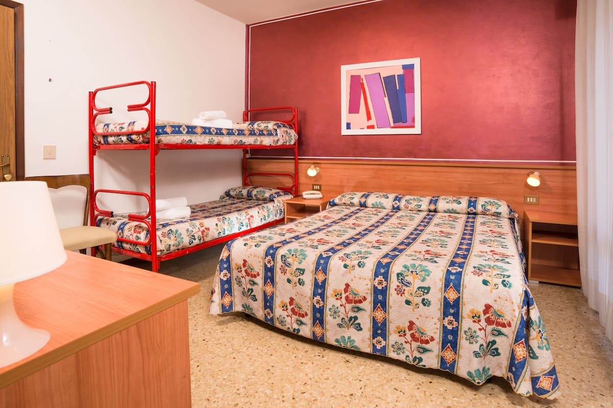 A hotel room with bunk beds, a wooden desk, a lamp, a nightstand, and a framed picture on the wall.