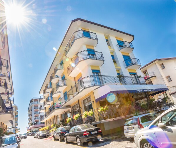 A multi-story hotel with balconies, a visible sign for 'Hotel Antille', and parked cars along the street.