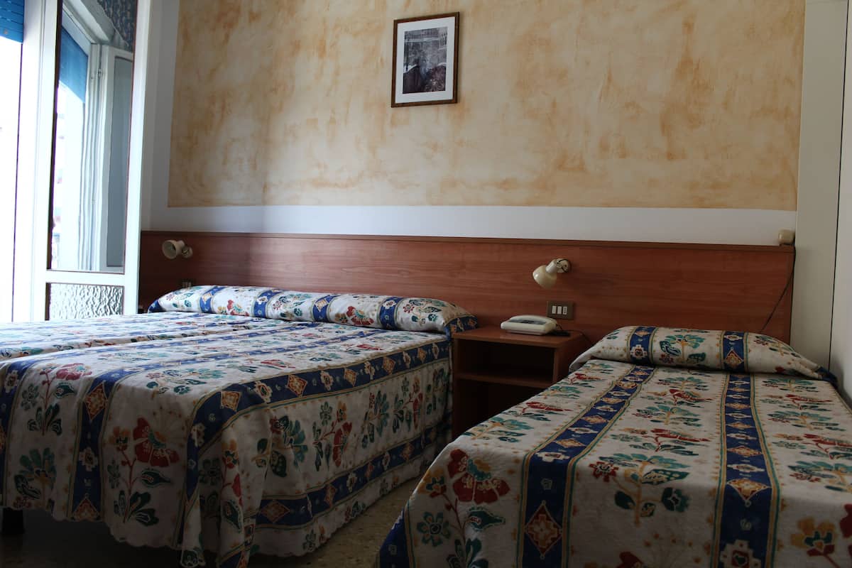 A hotel room with two beds, a wooden headboard, a bedside table with a lamp, and a framed picture on the wall.
