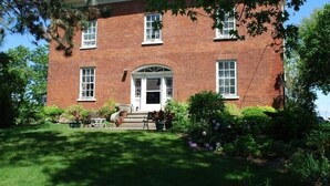 A brick building with a central entrance, surrounded by a well-maintained garden with various plants and a lawn.