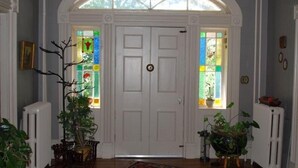 A room with a white door, two windows with colorful stained glass, and potted plants.