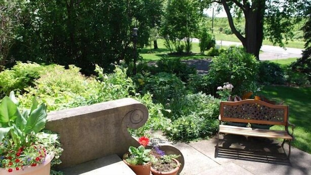 A garden area with a stone bench and a wooden bench, surrounded by various potted plants and greenery.
