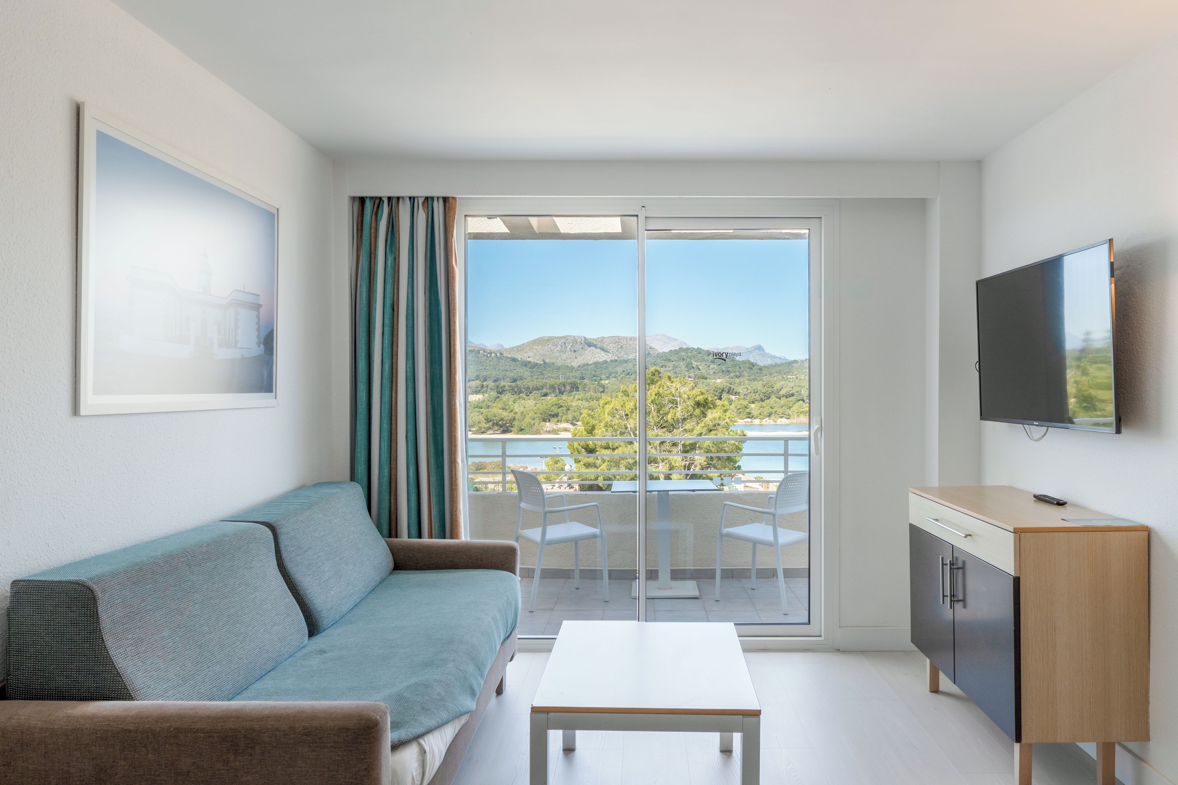 Una habitación moderna con sofá, televisor de pantalla plana, mesa de comedor y vistas a un paisaje montañoso a través de una puerta corrediza de vidrio.