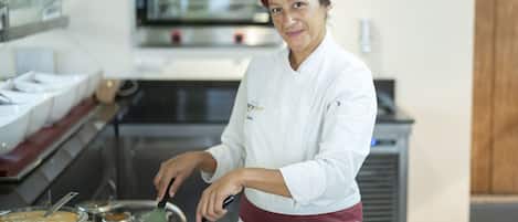 A chef in a white uniform and maroon hat cooking on a griddle in a kitchen.
