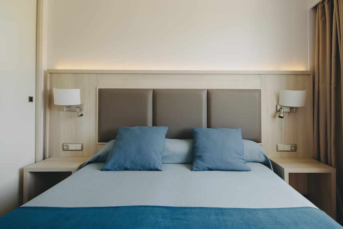 Une chambre d’hôtel avec un grand lit, deux tables de chevet et des lampes fixées au mur.