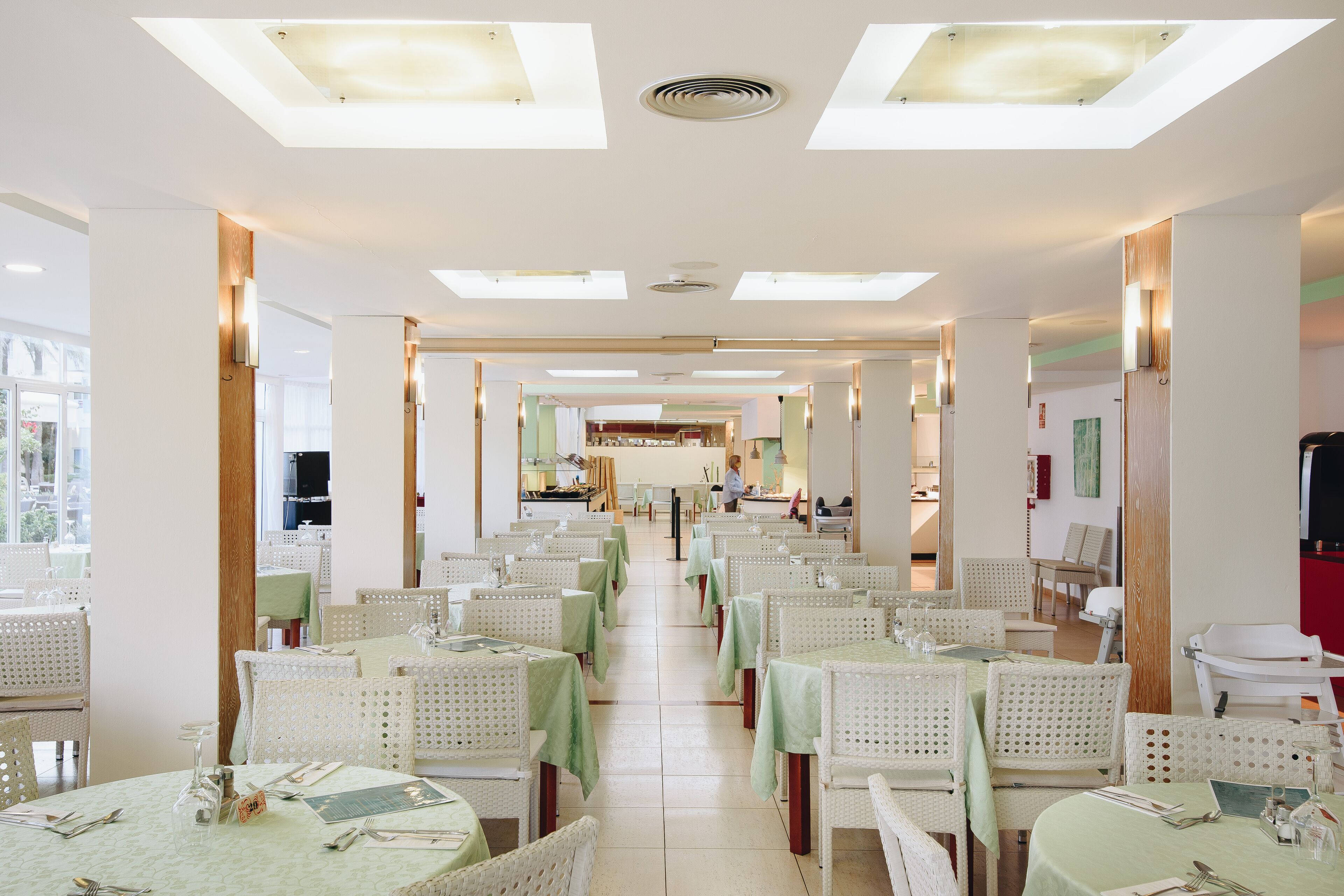 Un restaurante espacioso con techos altos, varias mesas y sillas dispuestas para comer.