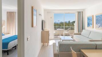 A hotel room with a bed, a desk, a sofa, and a balcony with a view of the sea and mountains.