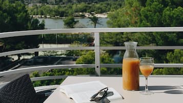 A table with a drink, a book, and glasses, overlooking a river and mountains.