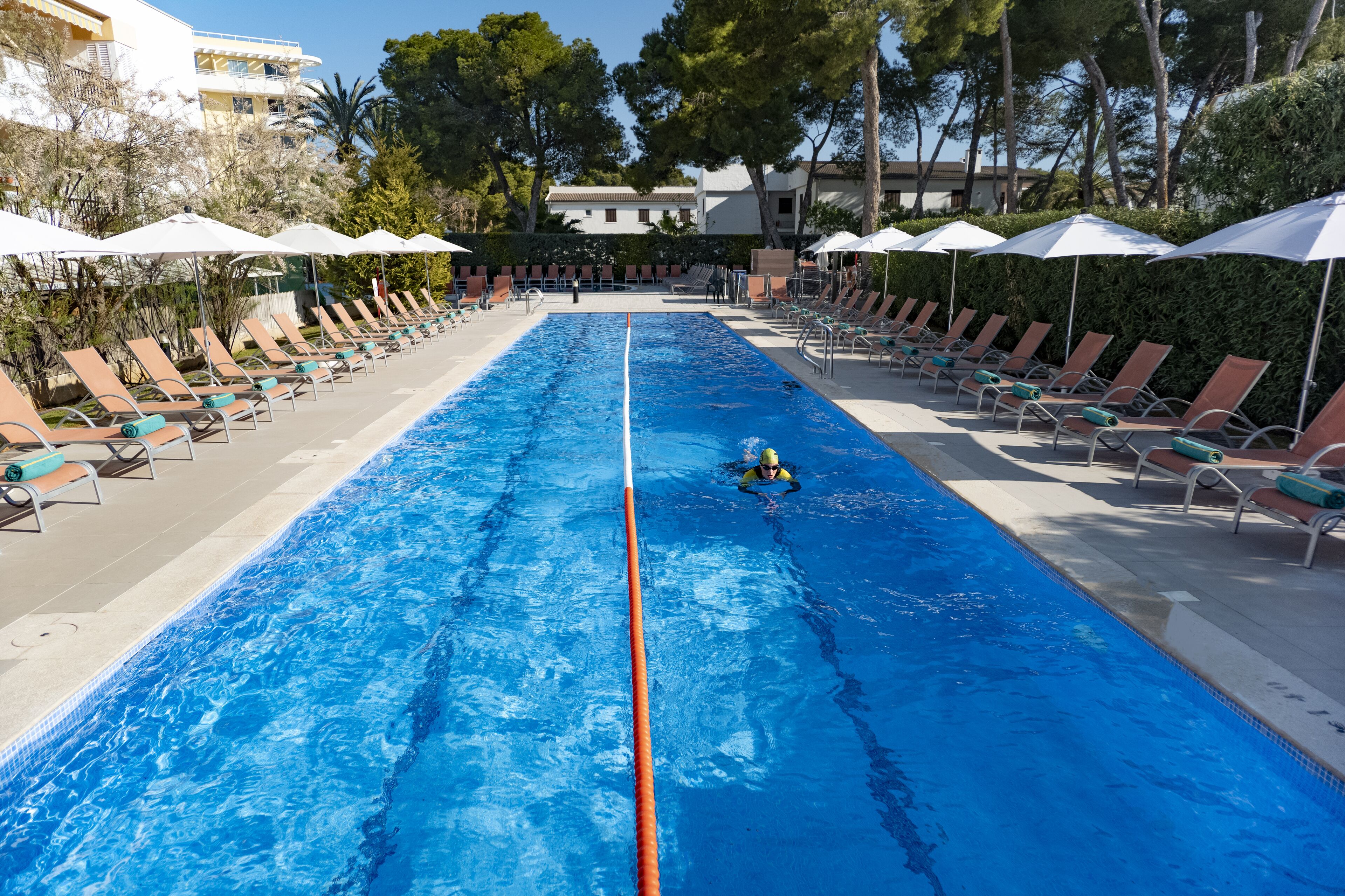 A swimming pool with lounge chairs and umbrellas, surrounded by trees and buildings.