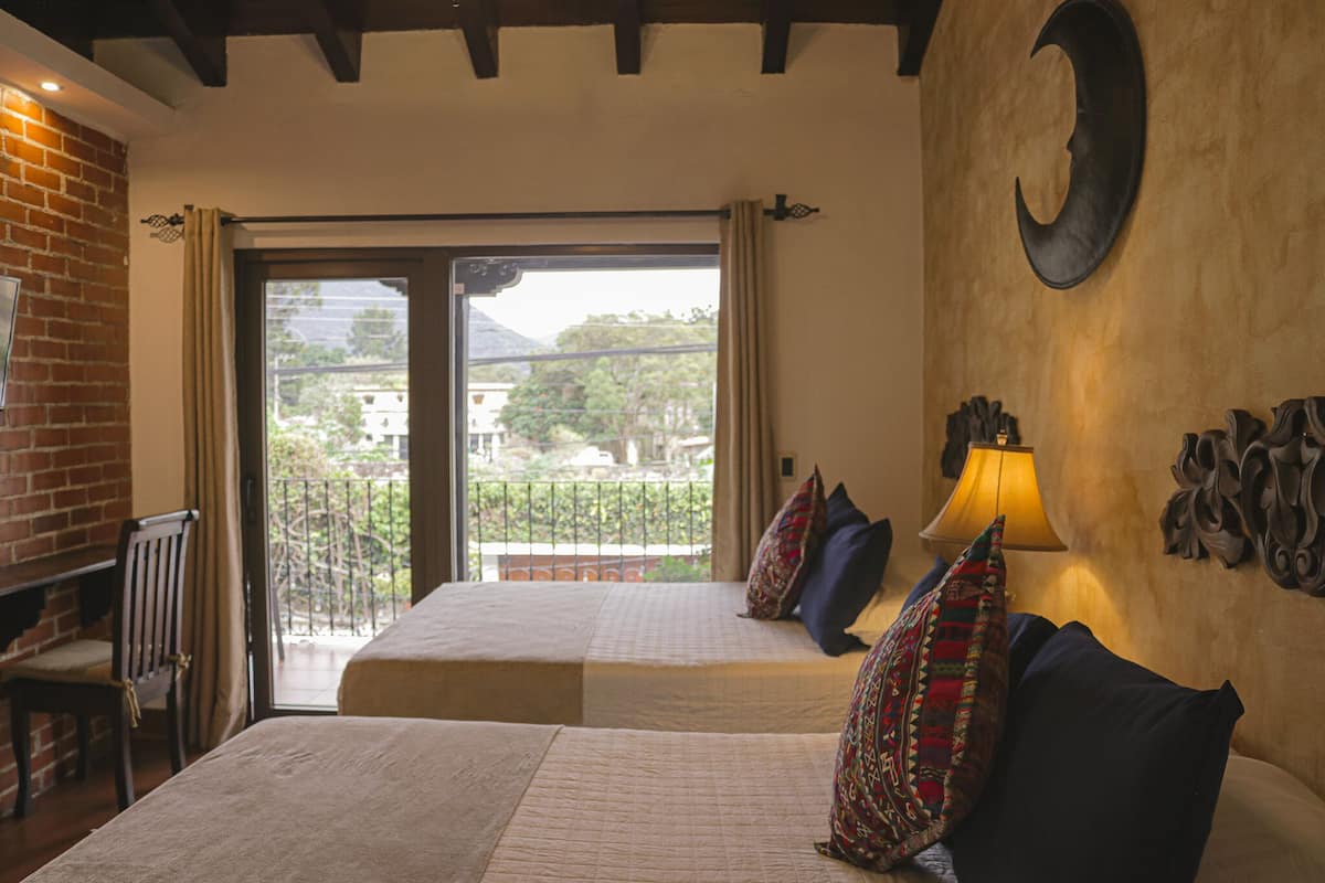 A hotel room with two beds, a balcony, a brick wall, and a large wall clock.
