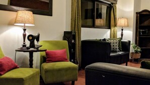 Una sala de estar acogedora con sillones verdes, un sofá negro y una mesita con una lámpara.