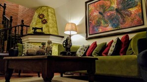Una sala de estar acogedora con un sofá verde, una mesa de centro de madera y una lámpara. Se ve una escalera al fondo.