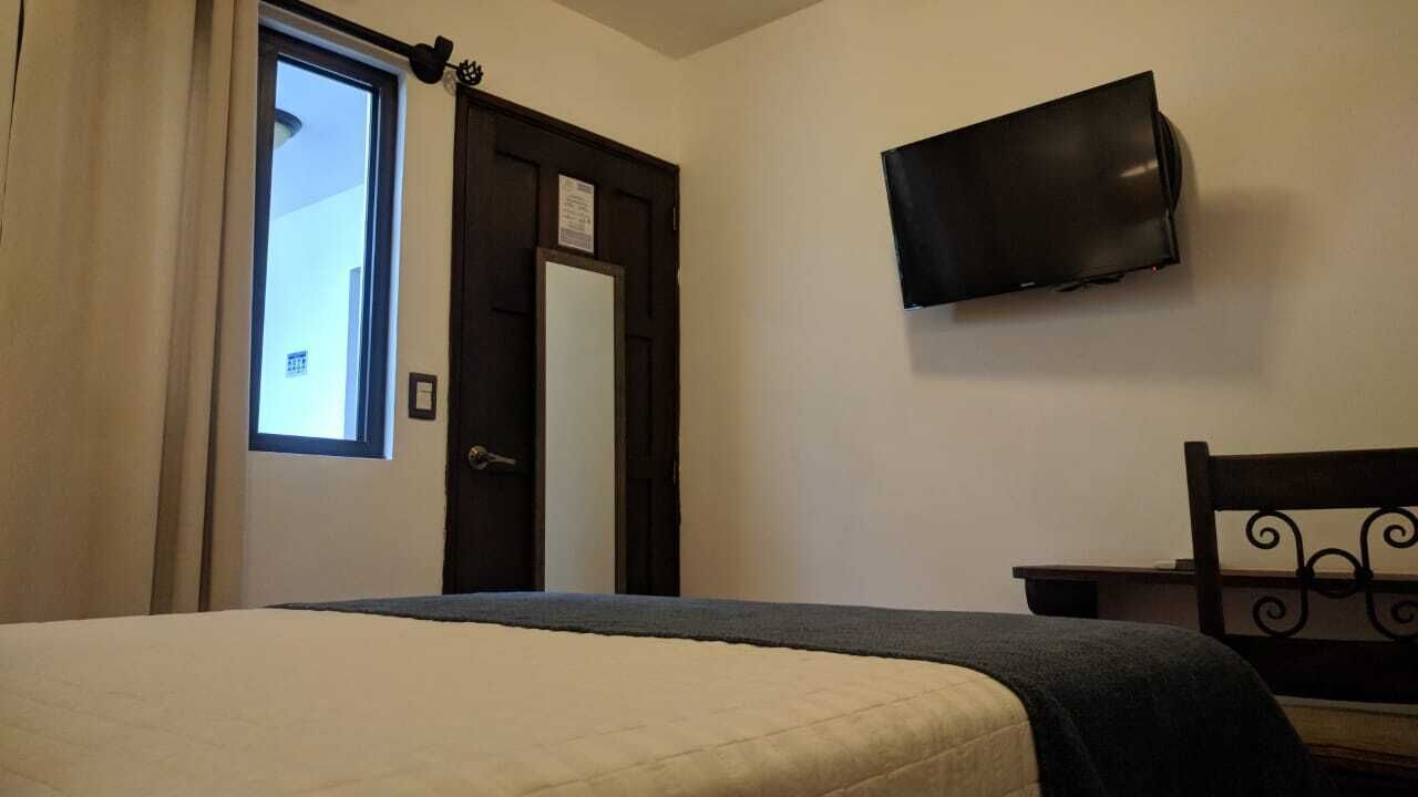 A bedroom with a bed, a television mounted on the wall, a door, and a window.