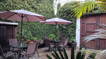 Un área de patio al aire libre con una mesa, sillas, dos sombrillas y una valla de madera.