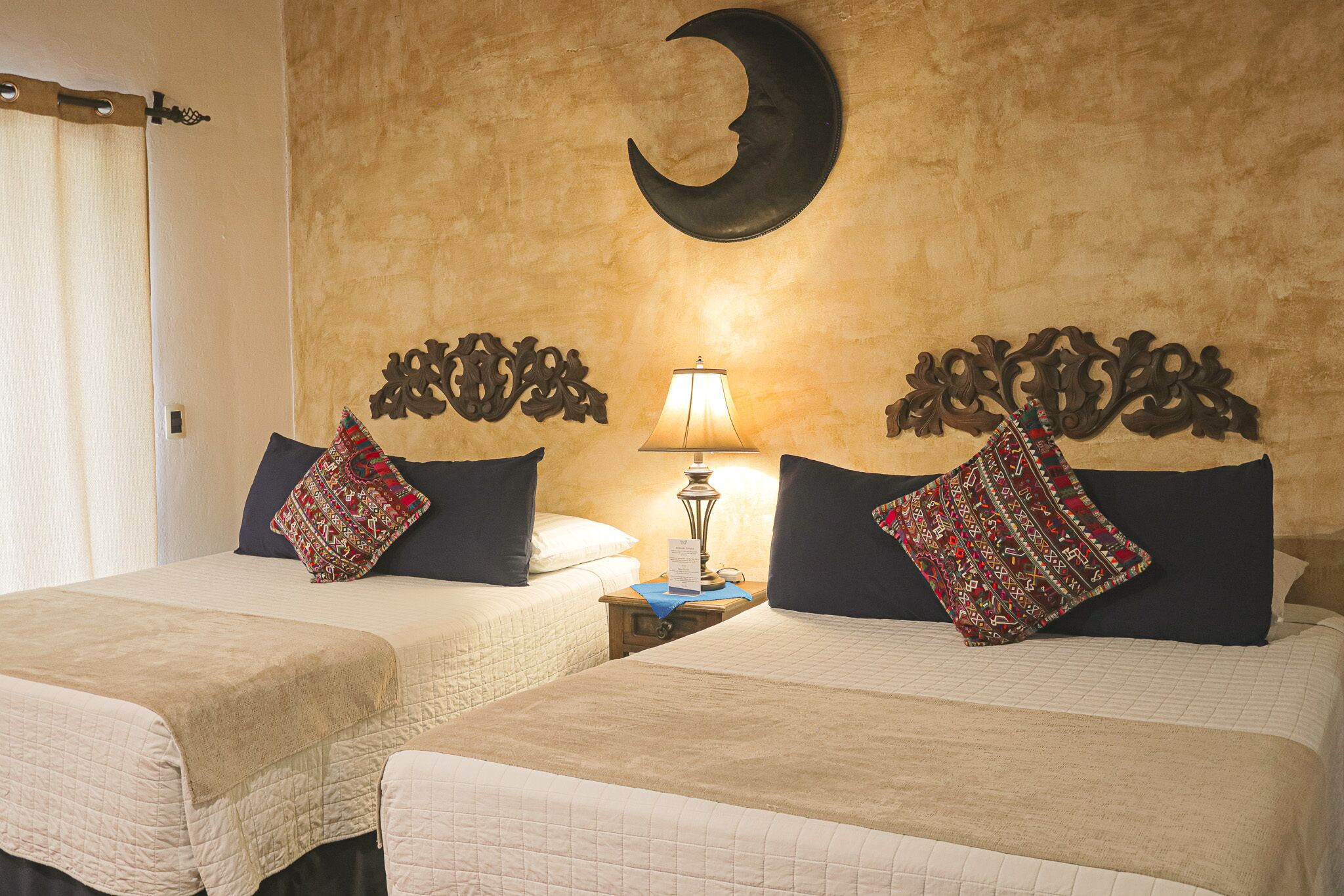 A hotel room with two beds, a nightstand with a lamp, and a crescent moon decoration on the wall.