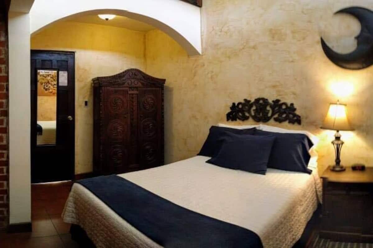A bedroom with a bed, a nightstand, a wall clock, and a door.