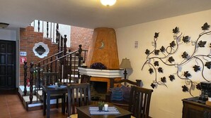 Un comedor con chimenea, sillas de madera, una mesa y una escalera que sube a otra habitación.
