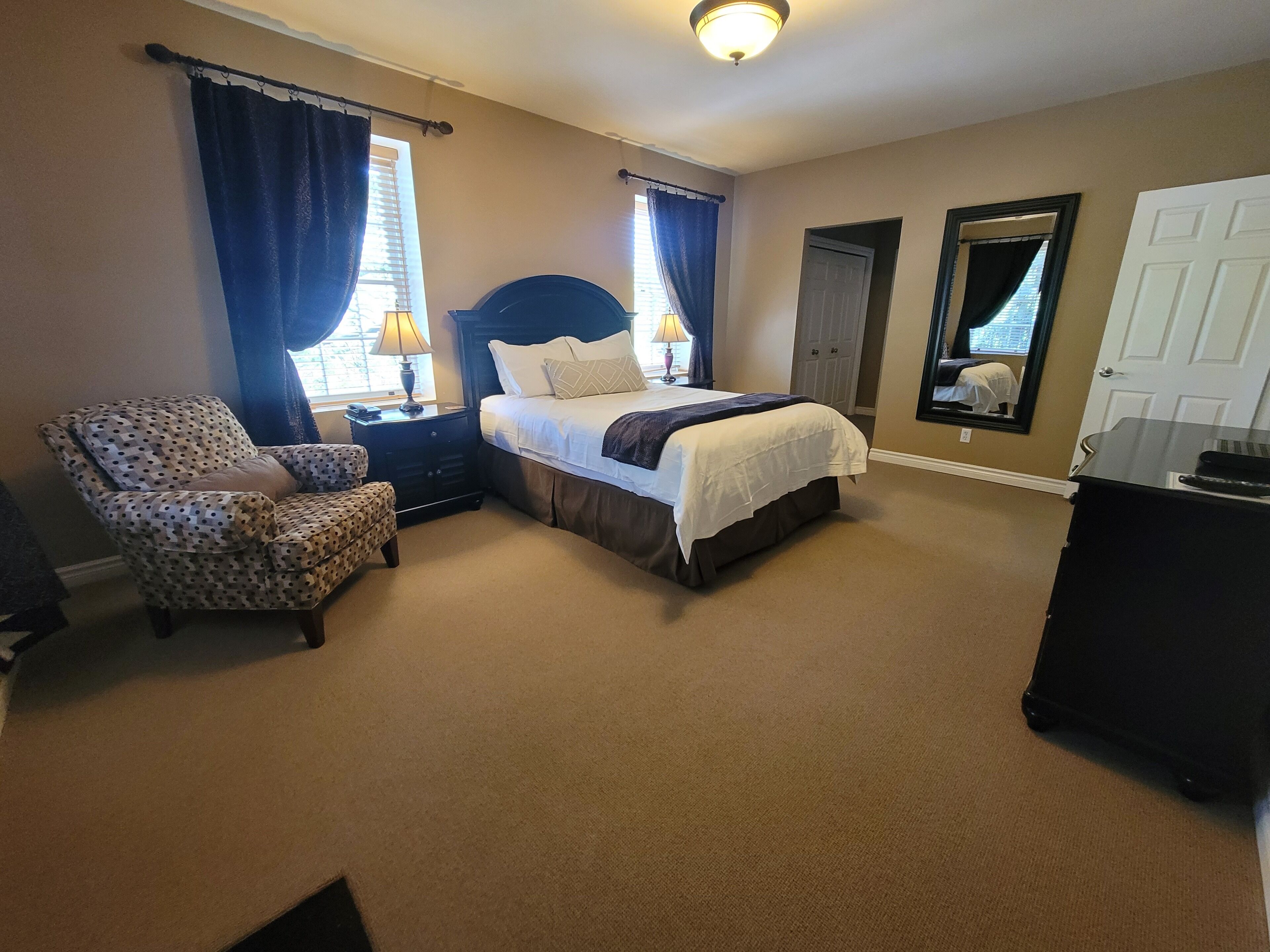 Una habitación de hotel con cama, una silla, cómoda y espejo.