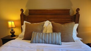 Ein ordentlich bezogenes Bett mit weißen Leinentüchern, einem Holz-Kopfende und mehreren Kissen, darunter eines mit Streifen.