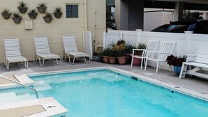Una piscina con sillas de descanso blancas y plantas en macetas alrededor.