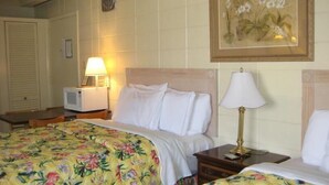 Una habitación de hotel con una cama, una mesita de noche con lámpara, un televisor y una colcha estampada con motivos florales.