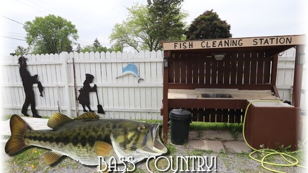 A fish cleaning station with a white picket fence, a large fish sculpture, and a sign that reads "FISH CLEANING STATION". - Twin Peaks Motel (Greater Napanee)