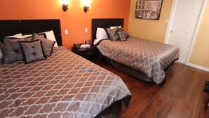 A hotel room with two beds, each with patterned bedding, a nightstand, and a wall-mounted lamp. - Twin Peaks Motel (Greater Napanee)