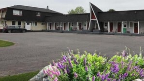 A motel with a row of rooms, a parking lot, and a flower bed in the foreground. - Twin Peaks Motel (Greater Napanee)
