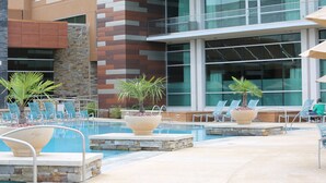 A pool area with lounge chairs, potted plants, and a modern building with large windows in the background. - Wind Creek Casino & Hotel Wetumpka (Wetumpka)