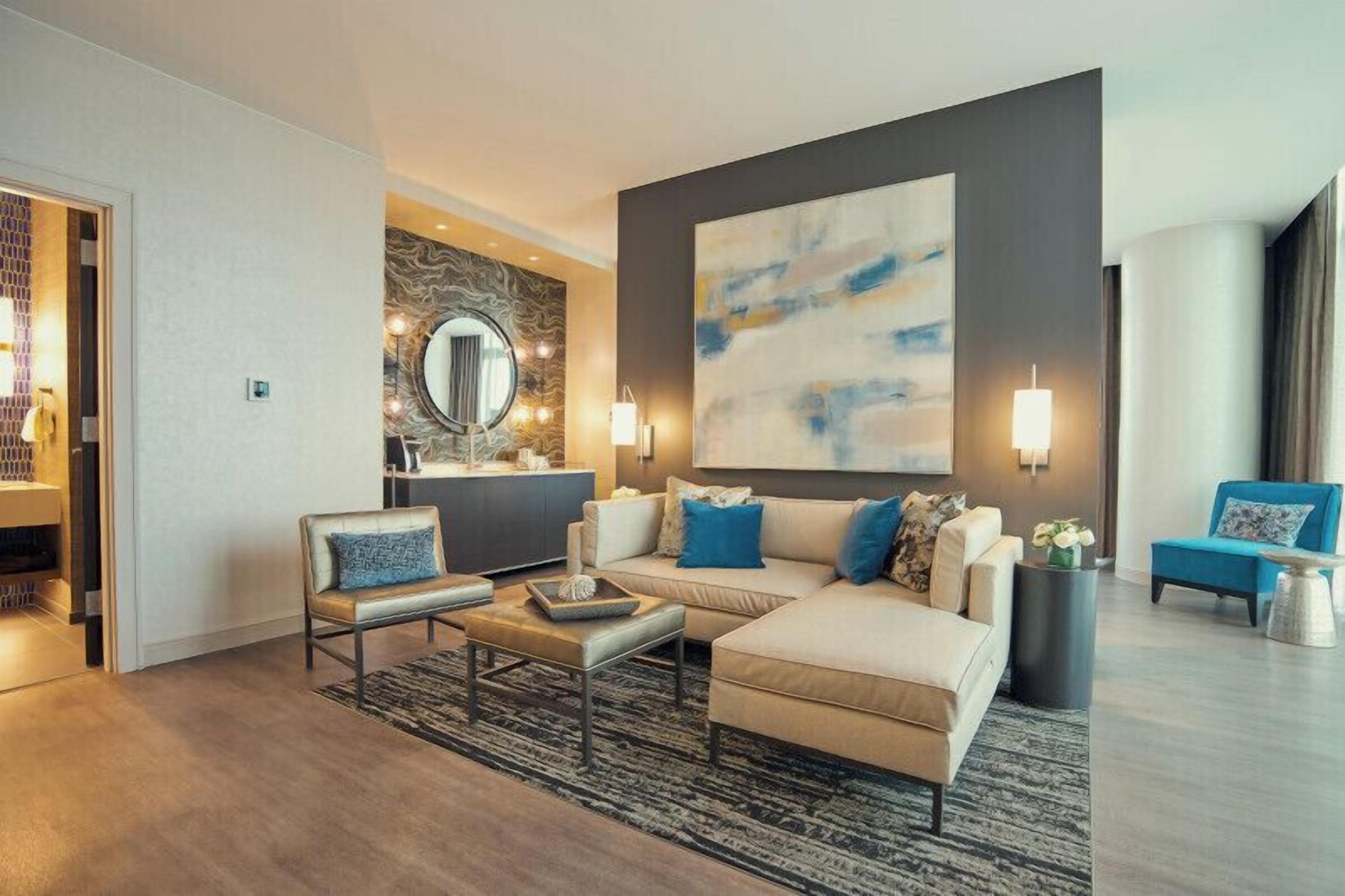 Una sala de estar moderna con un sofá, sillones, una mesita de centro y un cuadro abstracto grande en la pared.