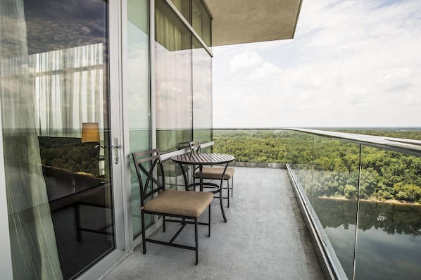 A balcony with a glass railing, a table, and two chairs.