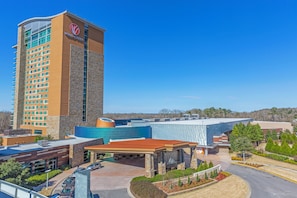 Un hotel con una torre destacada que muestra un logotipo, una zona de estacionamiento y un patio ajardinado.