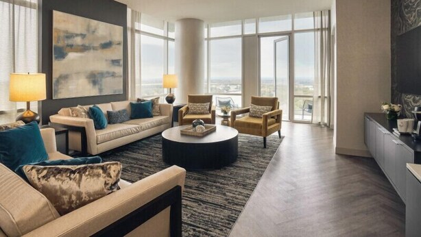 A modern living room with a sofa set, a coffee table, and two armchairs. There is a large window providing a view of the city. - Wind Creek Casino & Hotel Wetumpka (Wetumpka)