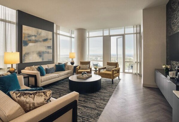 A modern living room with a sofa set, a coffee table, and two armchairs. There is a large window providing a view of the city. - Wind Creek Casino & Hotel Wetumpka (Wetumpka)