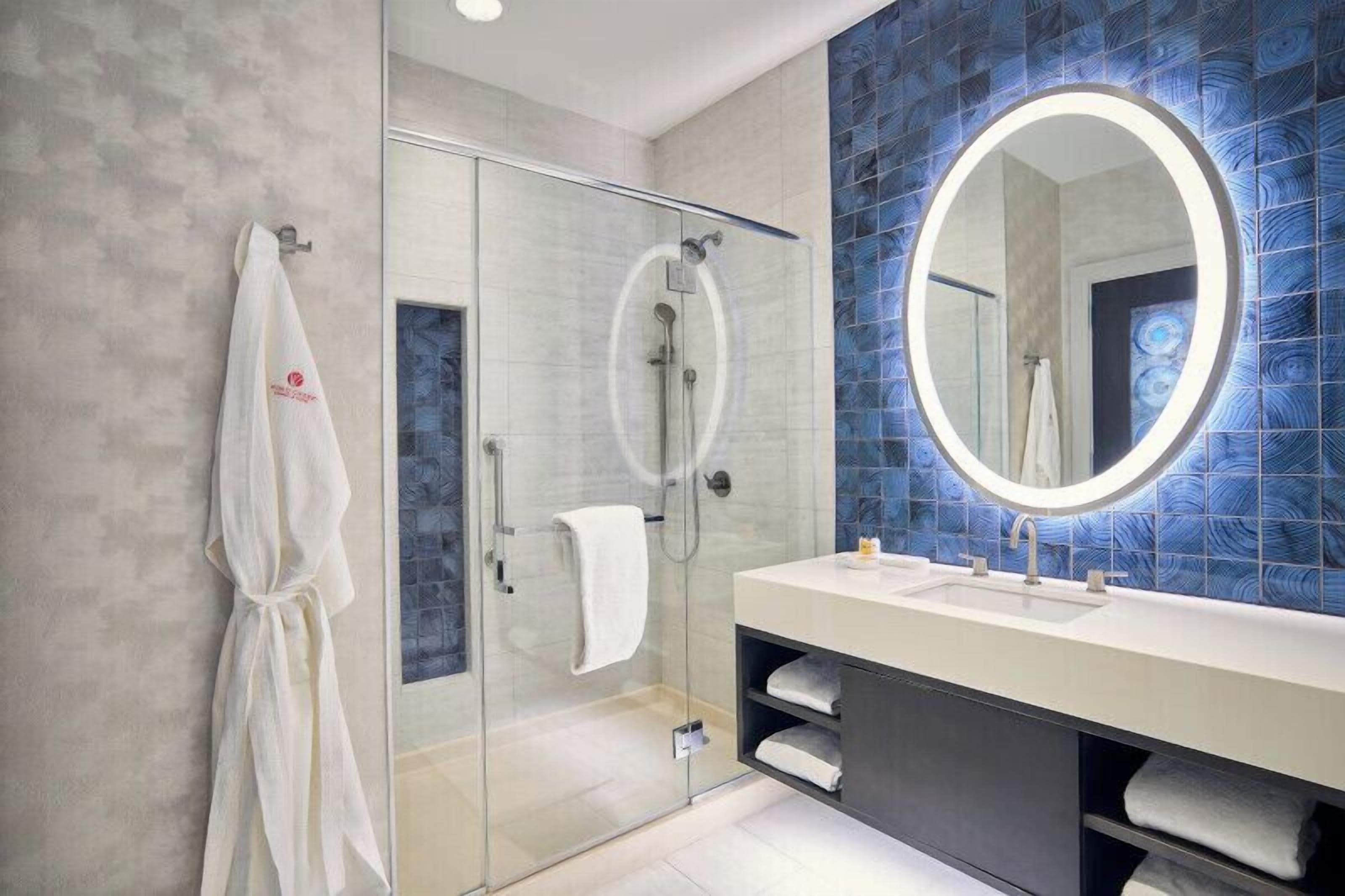 A modern bathroom with a glass shower enclosure, a large mirror, and a white vanity with a sink.