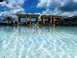 Una piscina cristalina con sillas de descanso y un área techada, bajo un cielo parcialmente nublado.