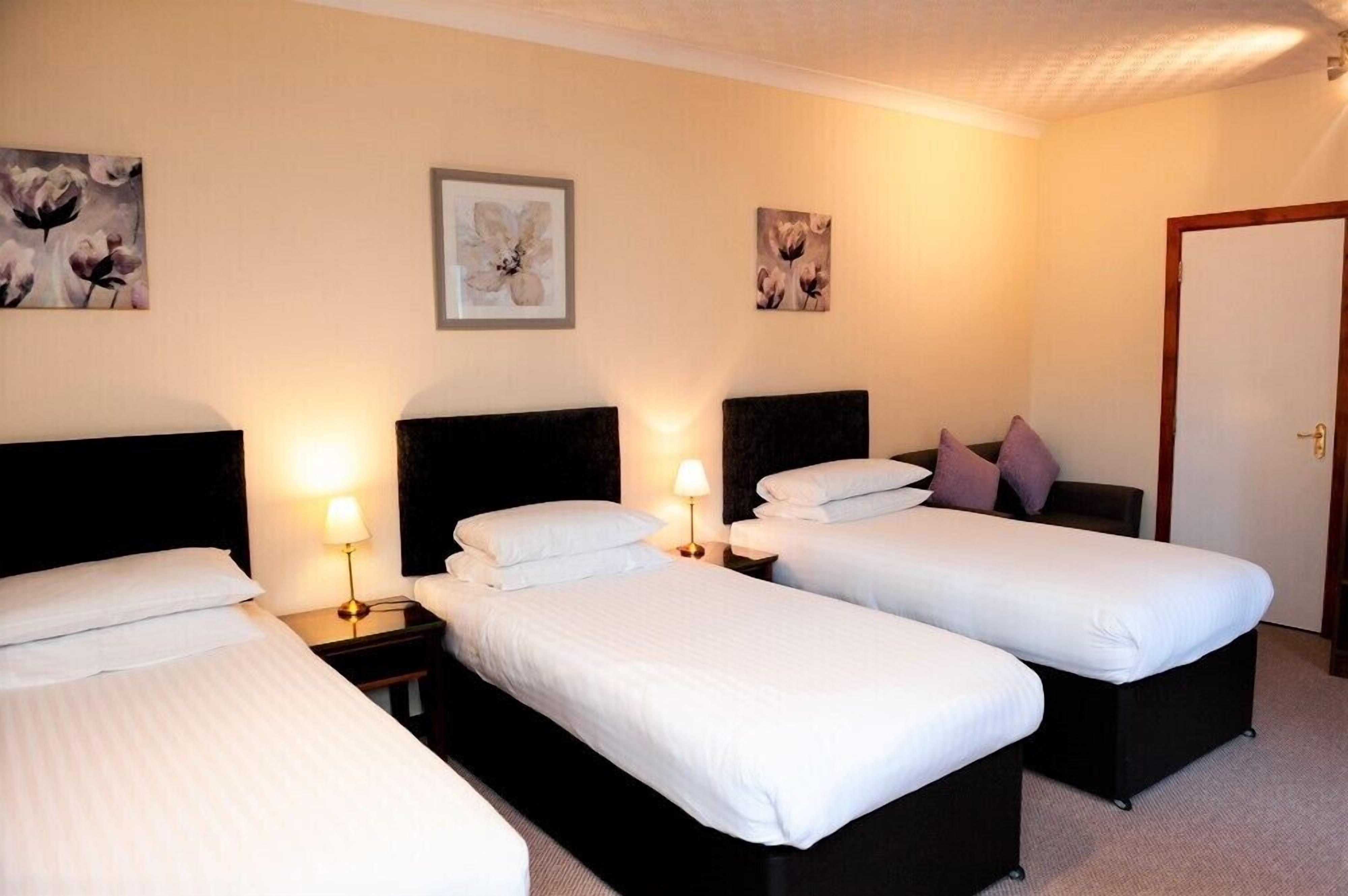 A hotel room with two single beds, a double bed, and a door.