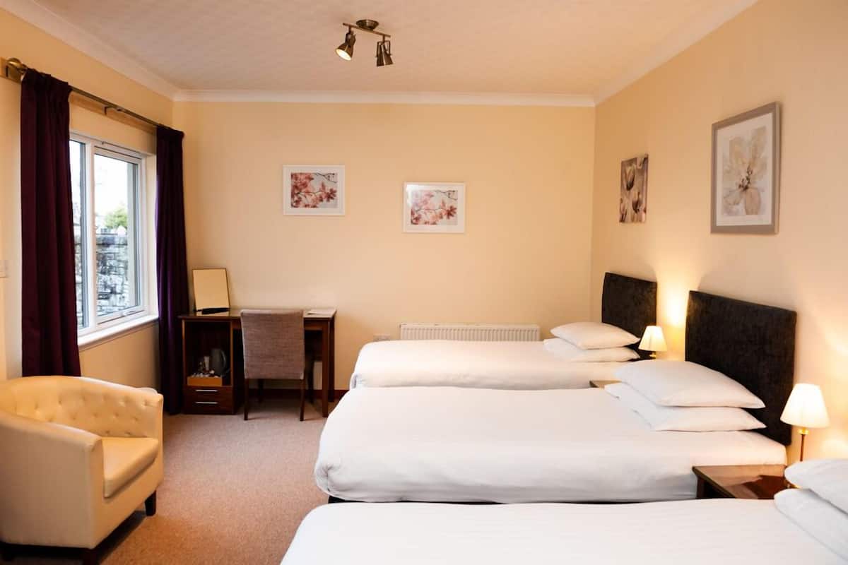 A hotel room with three beds, a desk, a chair, and artwork on the walls.